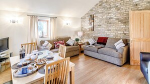A cozy living room with a brick wall, wooden furniture, and a dining area with a table set for two. - Brook House Farm Cottage (Scamblesby, near Louth)