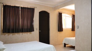 Una habitación con dos camas, una puerta y un ventanal con cortinas.