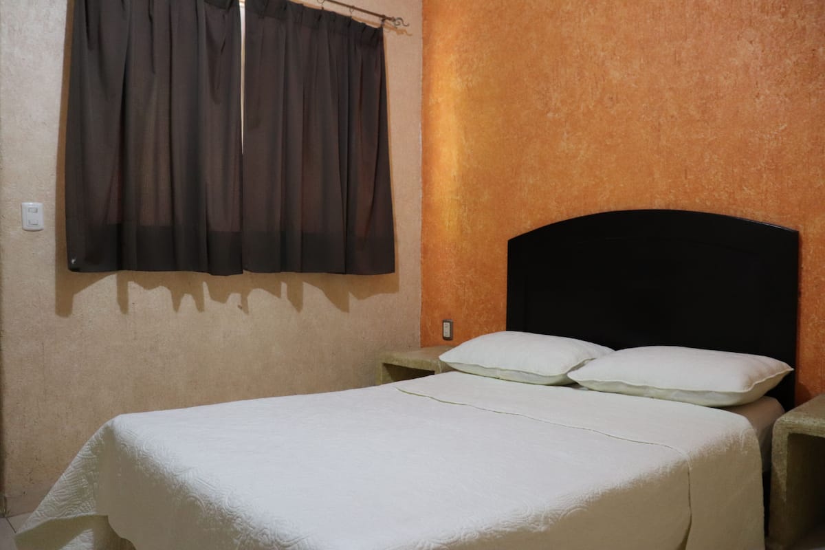 A single bed with a white bedspread, a black headboard, and a nightstand with two white pillows.