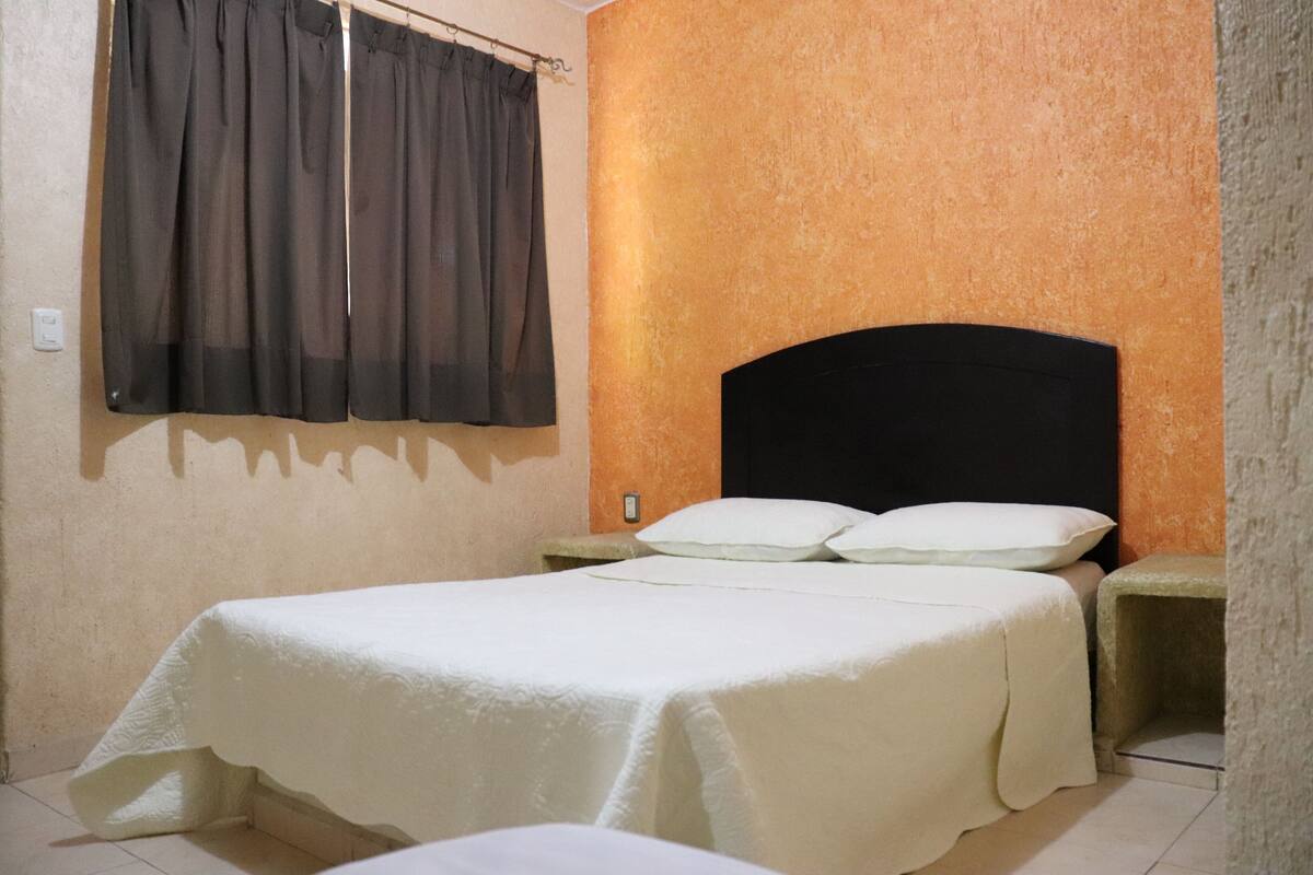 A single bed with a white bedspread in a room with an orange textured wall and a black headboard.