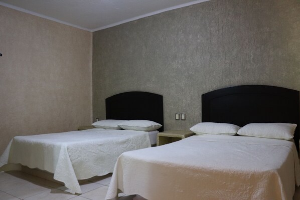 Una habitación con dos camas, cada una con cabecero y ropa de cama blanca.
