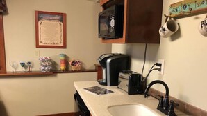 A kitchen with a white sink, a toaster, a microwave, and a coffee maker. There is a wooden shelf with decorative items and a framed notice on the wall. - Serenity Suite-Private Suite close to downtown (Estes Park)