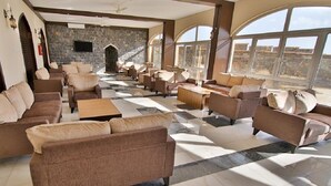 A spacious lobby with multiple seating areas, a stone wall, and large windows offering a view. - Sama Hotel Al Jabal Akhdhar (Sayq)