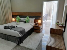 A modern hotel room with a large bed, two bedside tables, a wooden nightstand, and a small desk with a lamp.