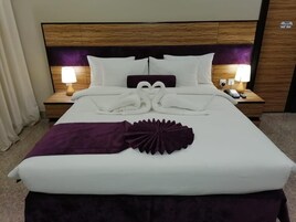 A neatly made bed with white linens, a purple throw blanket, and a decorative fan. There are two bedside lamps and a phone on the nightstand.