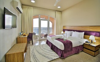 Habitación de hotel con una cama grande, un escritorio, una silla, un televisor y un balcón con vistas.