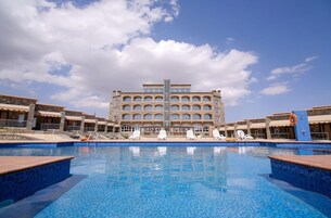 A hotel with a large pool, multiple lounge chairs, and a central building with a distinctive architectural design.
