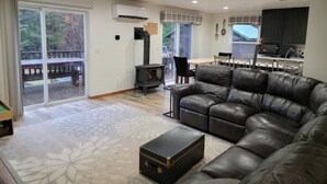 A living room with a leather sofa, a fireplace, a dining area, and a kitchen with dark cabinets. - Cozy Cabin with hot tub, Sauna & outdoor kitchen! (Ronald)