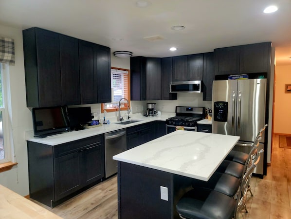 A modern kitchen with dark cabinets, a stainless steel refrigerator, a microwave, and a stove.