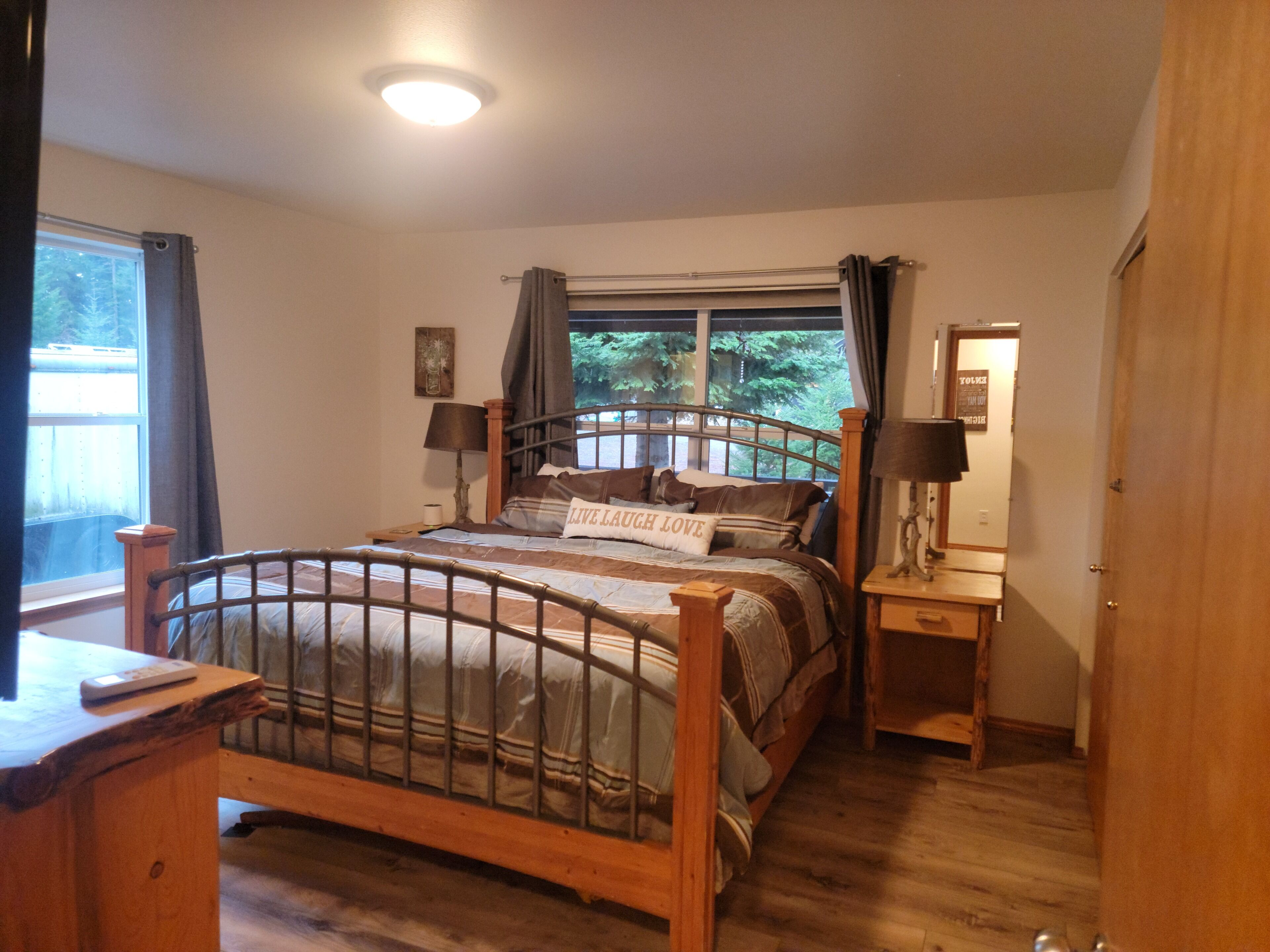 Un dormitorio con cama de madera, mesitas de noche, una ventana con cortinas y una mesita auxiliar.