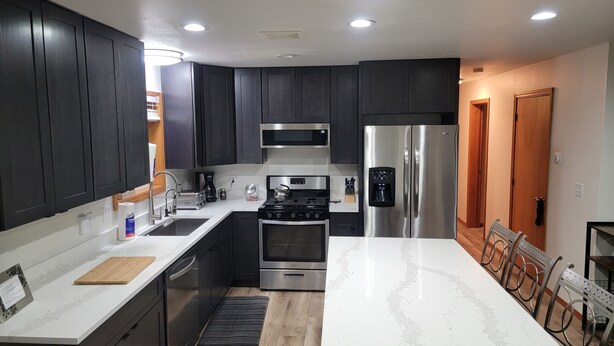 A modern kitchen with dark cabinets, stainless steel appliances, and a marble countertop. - Cozy Cabin with hot tub, Sauna & outdoor kitchen! (Ronald)