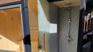 A modern outdoor shower with a glass door, a wooden deck, and a stone wall. - Cozy Cabin with hot tub, Sauna & outdoor kitchen! (Ronald)