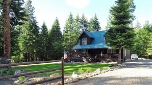 A cabin with a metal roof, surrounded by a gravel driveway and a wooden fence. - Cozy Cabin with hot tub, Sauna & outdoor kitchen! (Ronald)