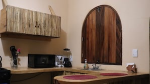 A kitchen with a wooden counter, a microwave, a coffee maker, and a wooden cabinet above the counter.