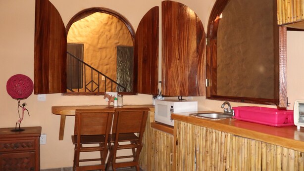 A kitchen with wooden cabinets, a microwave, a sink, and a dining area with two chairs.