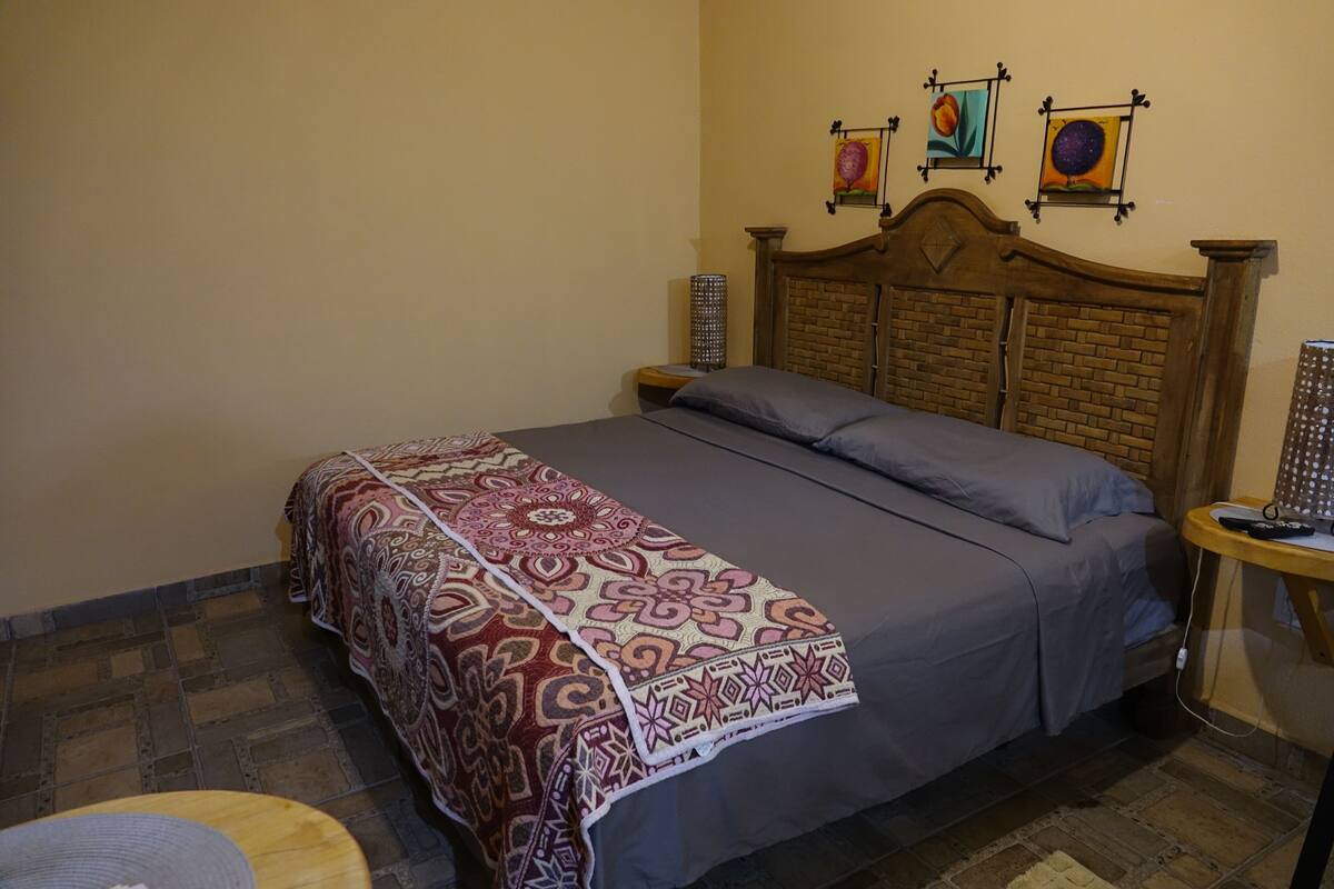 A bedroom with a bed, a bedside table, and a wall with three framed artworks.