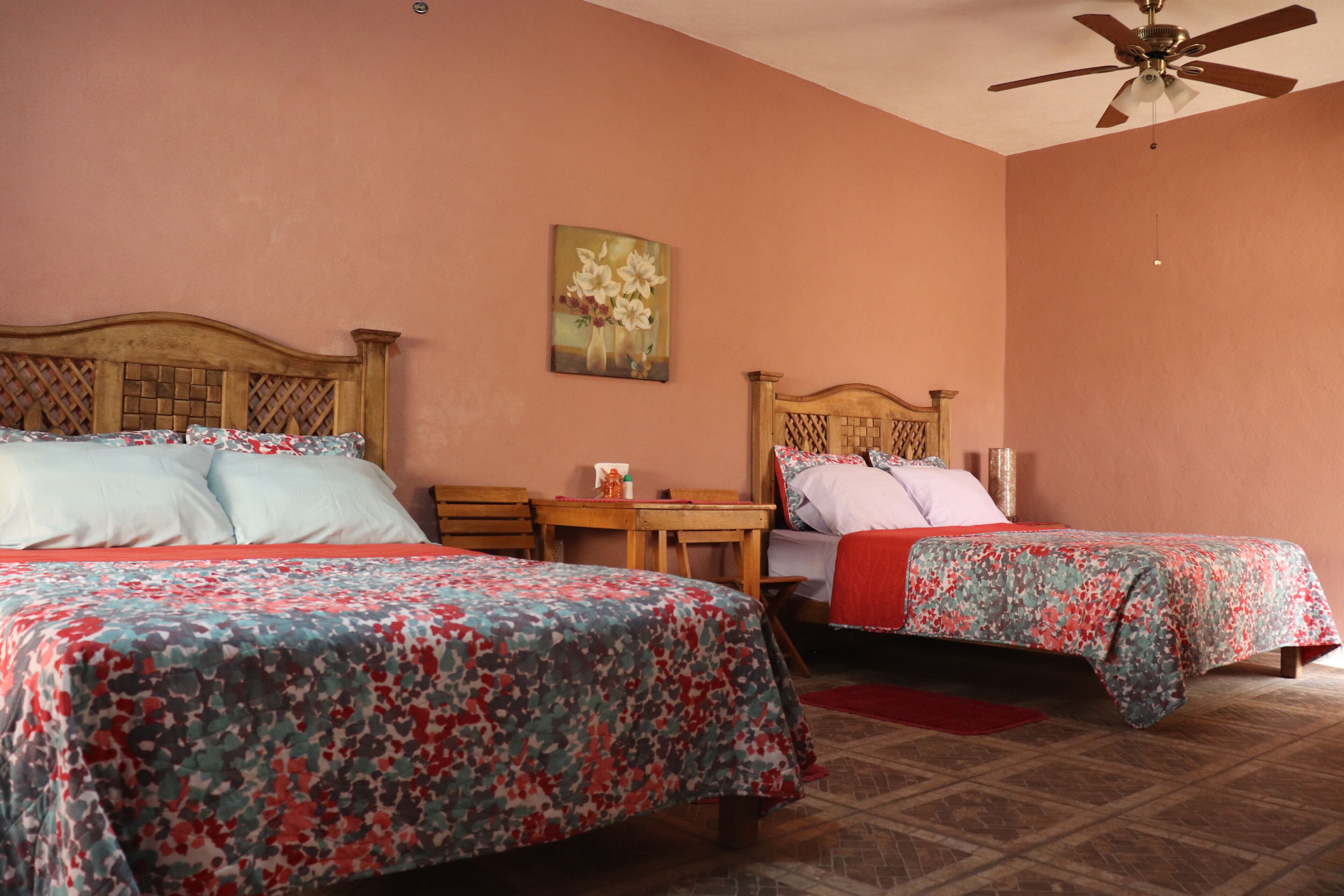 A bedroom with two beds, a wooden headboard, a ceiling fan, a small table, and a painting on the wall.