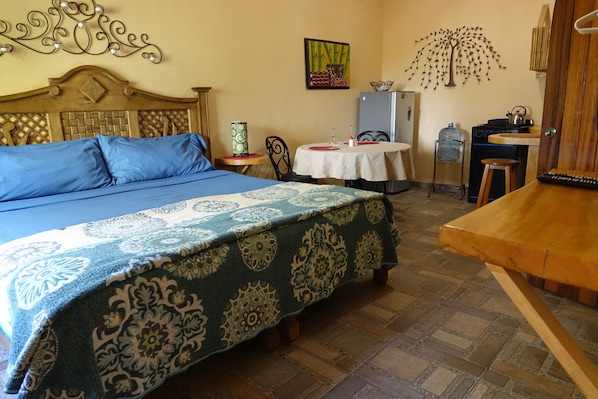 A room with a bed, a table, chairs, a refrigerator, and a wall with decorative items.
