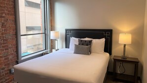 A hotel room with a large bed, two bedside lamps, a brick wall, and a window.