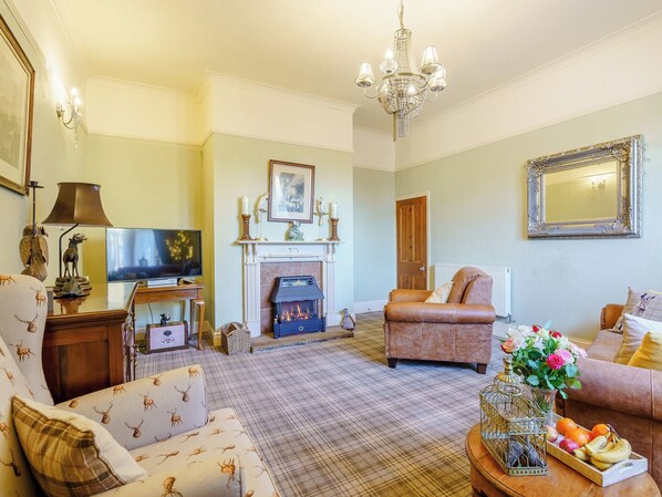A living room with a fireplace, a television, a sofa, and a coffee table with fruit.