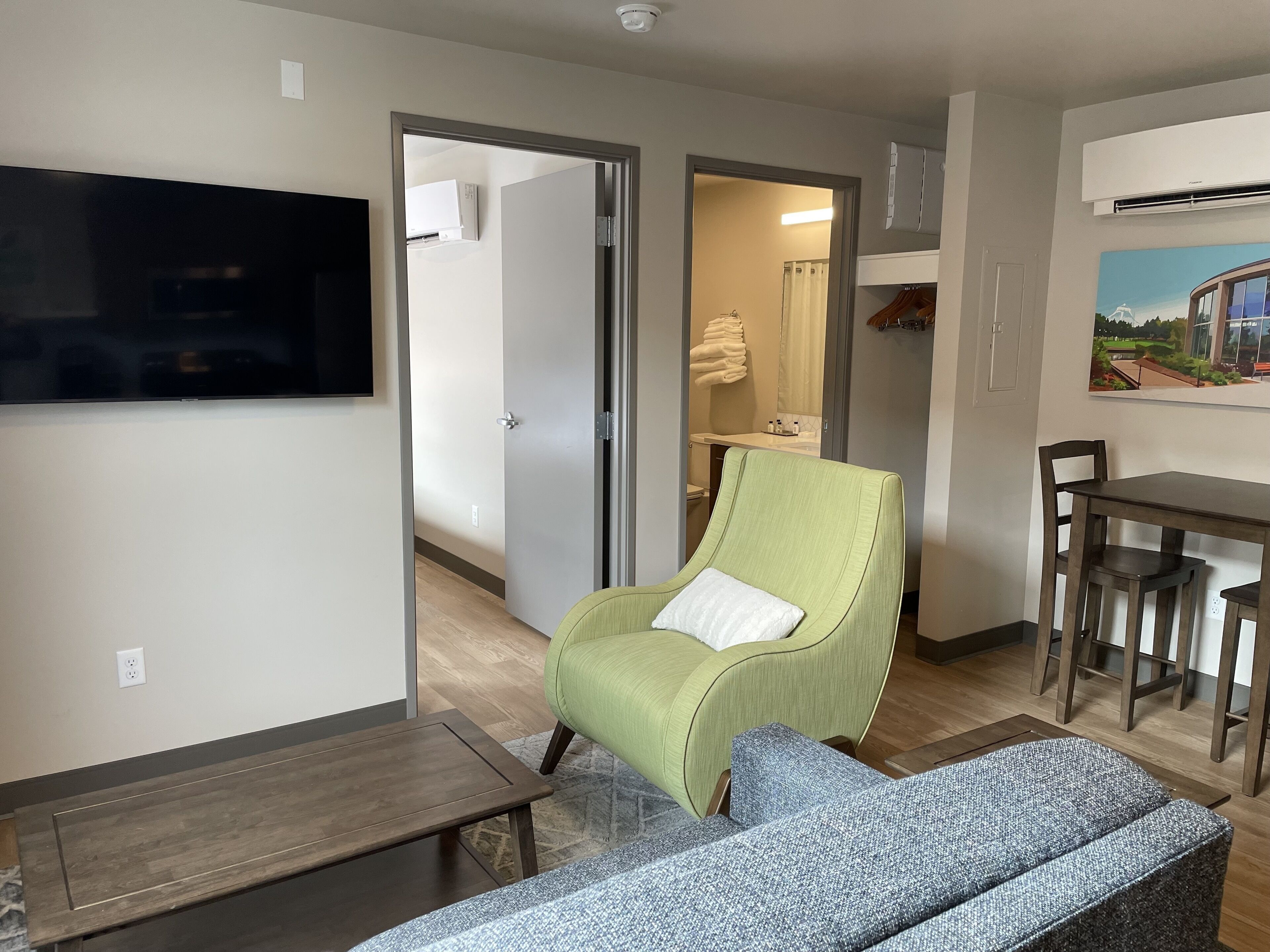 A modern living room with a green armchair, a blue sofa, a wooden coffee table, and a TV mounted on the wall.