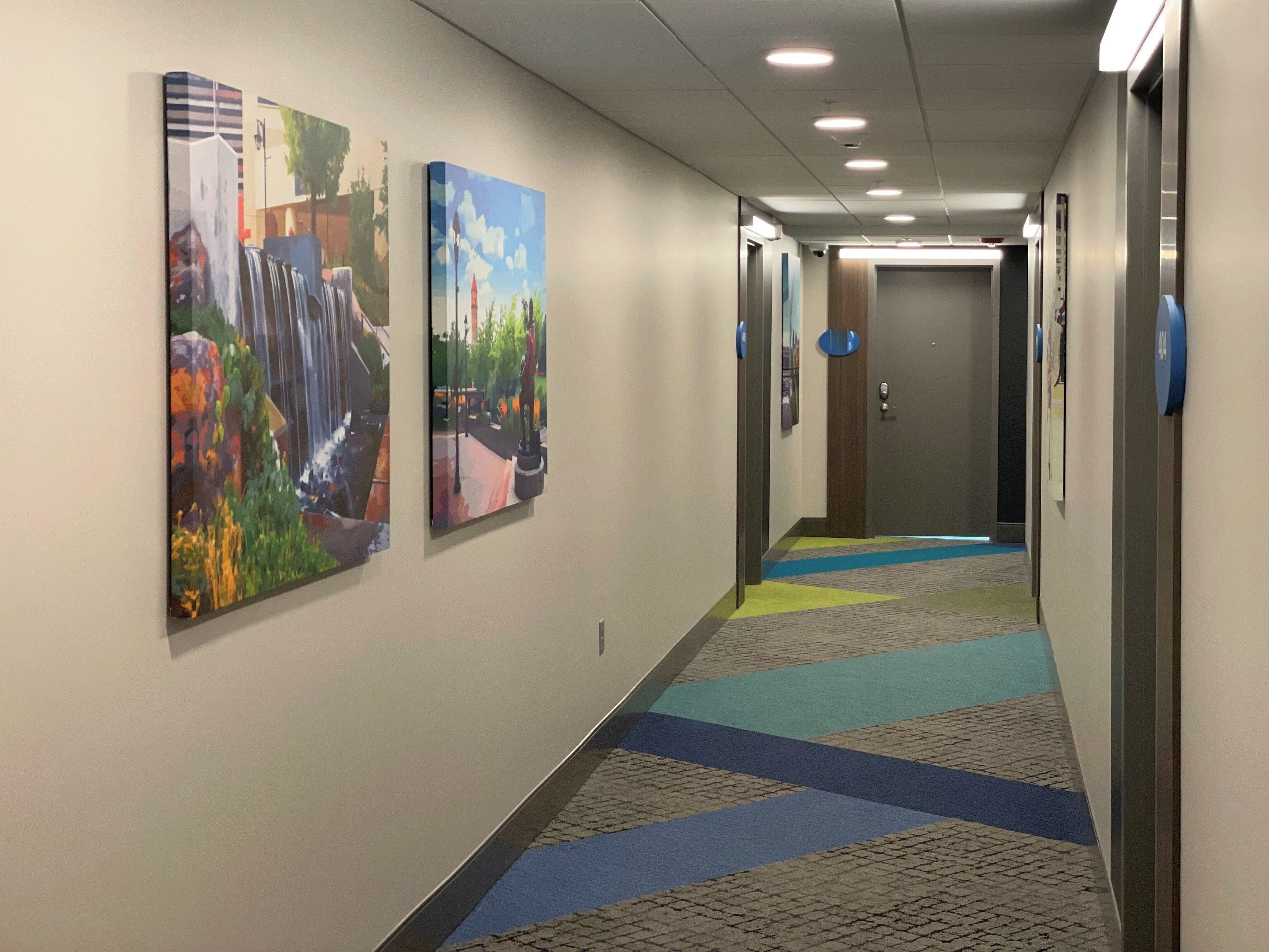A hallway with two paintings on the walls, a patterned carpet, and a door at the end.