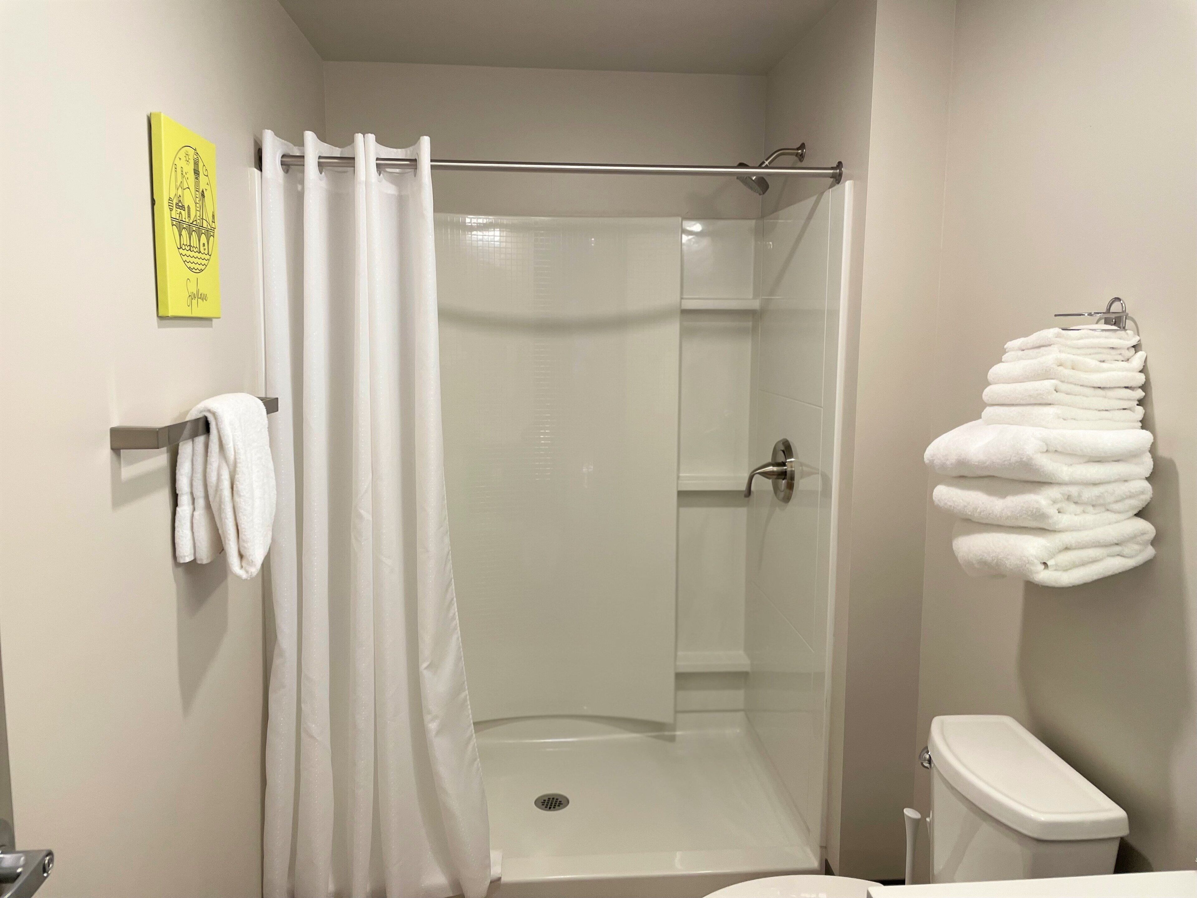 A shower area with a glass door, a white towel rack, and a stack of white towels on a hook.