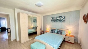 Une chambre à coucher comprenant un lit, des tables de chevet, un miroir, une armoire et une œuvre d’art murale.