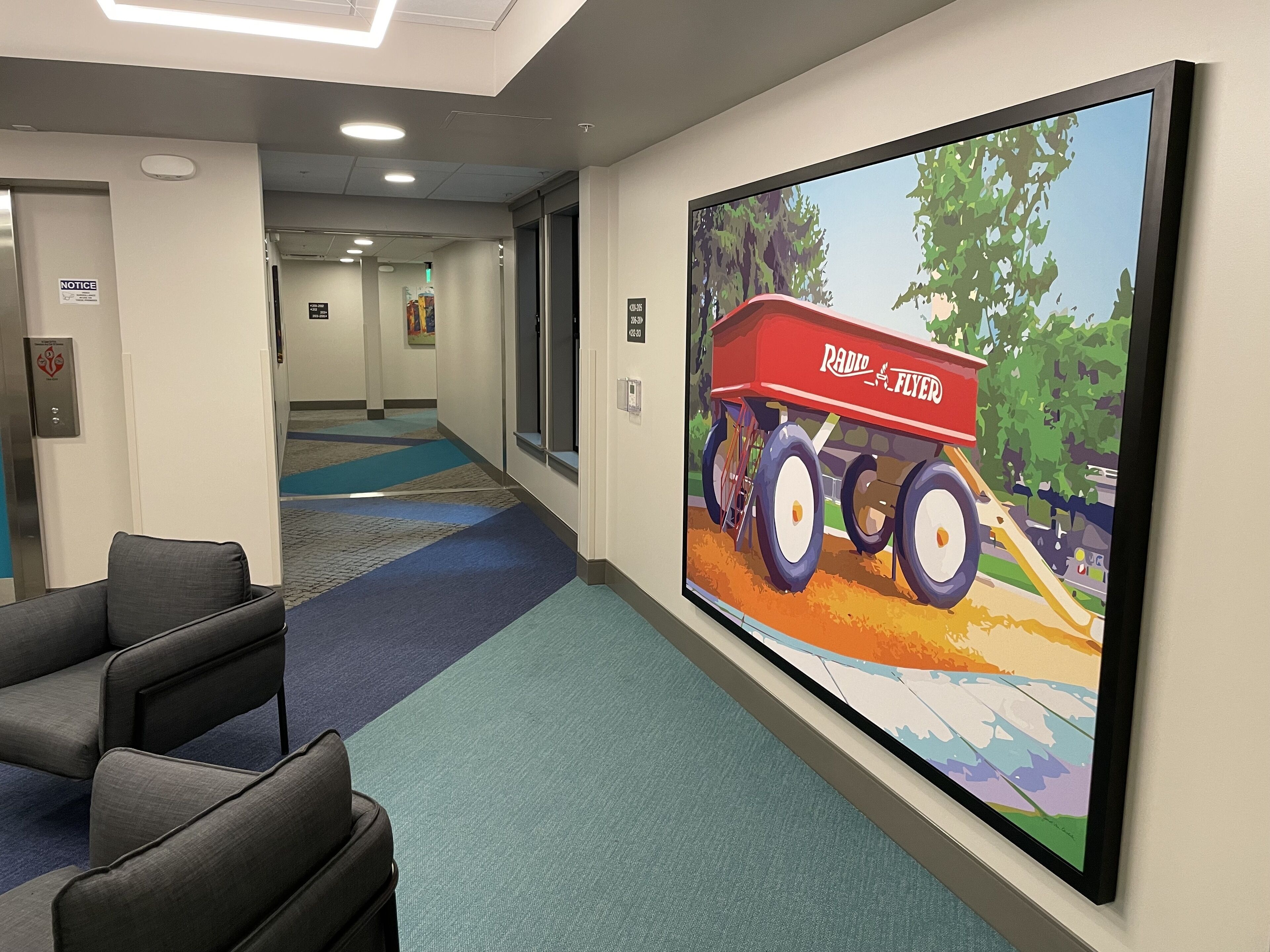 A hallway with a large painting of a red tractor, a reception desk, and a sign indicating a notice.