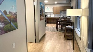 A modern kitchen with wooden cabinets, a dining area with a table and chairs, and a hallway with a door leading to another room.