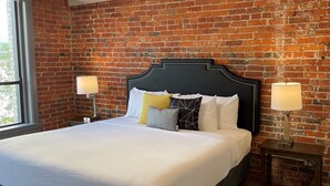 Une chambre d’hôtel avec un mur en briques, un grand lit avec une literie blanche, deux lampes de chevet et une fenêtre.