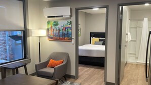 Ein Hotelzimmer mit einem Bett, einem Sessel mit orangefarbenem Kissen, einem Schreibtisch, einer Lampe und einem Bild an der Wand.
