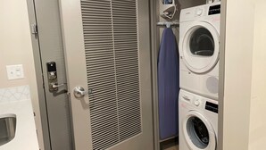 A laundry room with a front-loading Bosch washer and dryer, a wall-mounted ironing board, and a door with a vented window.