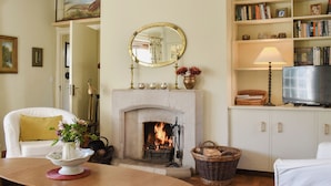 Een gezellige woonkamer met een open haard, een witte bank, een houten tafel en een boekenkast vol boeken en decoratieve objecten.