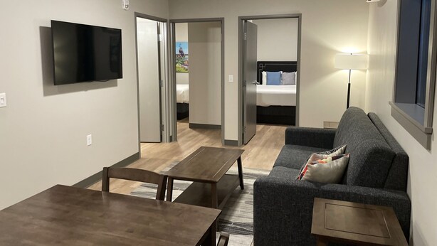 A modern living room with a flat-screen TV, a sofa, a coffee table, and a dining table.