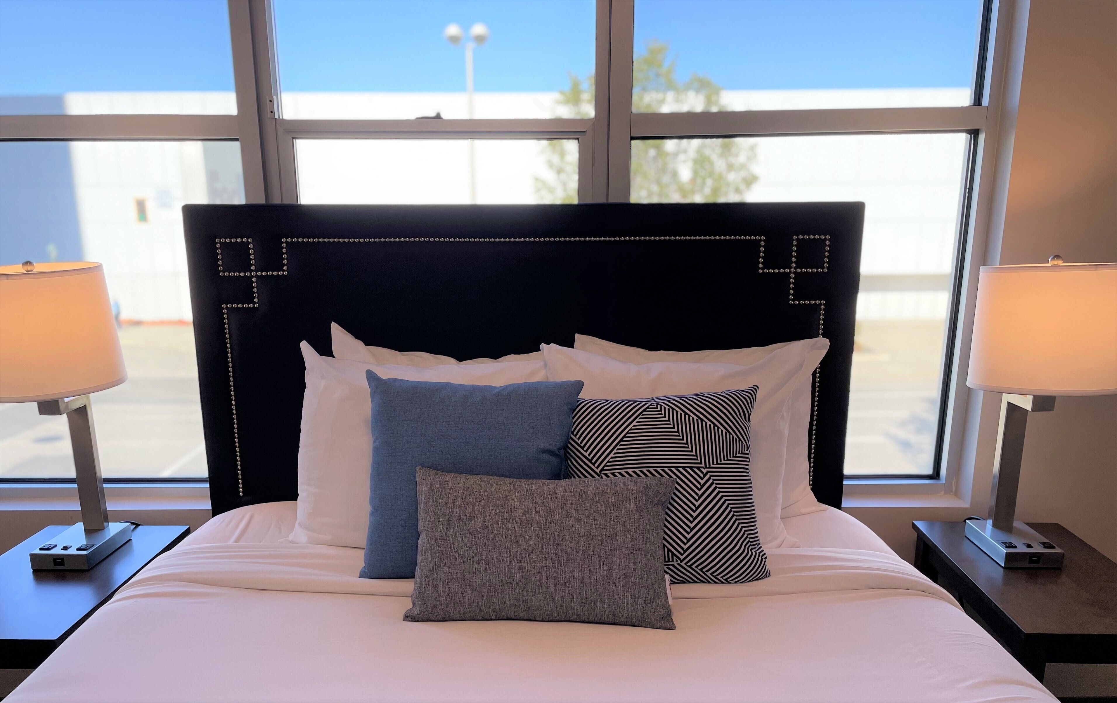 A hotel room with a bed, pillows, and two bedside lamps.