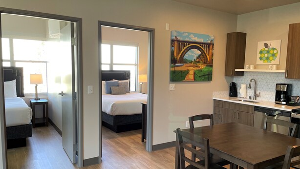 A hotel room with a bed, bedside table, lamp, and a painting of a bridge.