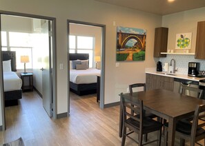 A hotel room with a bed, bedside table, lamp, and a painting of a bridge.