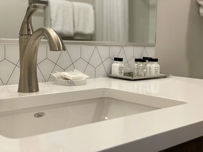 A modern bathroom with a large sink, a chrome faucet, and a mirror above it. There are toiletries on the sink counter.