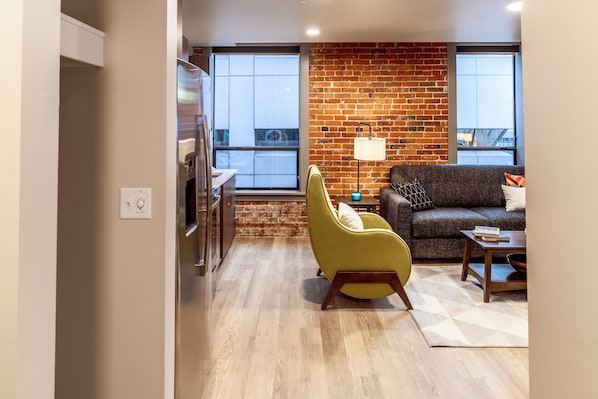 A modern living room with a brick accent wall, a sofa, a yellow armchair, and a coffee table.