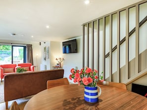 A modern living room with a wooden dining table, a red sofa, and a staircase with striped walls.
