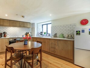 Una cocina moderna con armarios de madera, una mesa de comedor con sillas, un refrigerador y un reloj en la pared.
