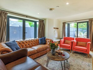 Una sala de estar con un sofá de cuero marrón, un sillón rojo y una mesa de centro con bebidas y flores.