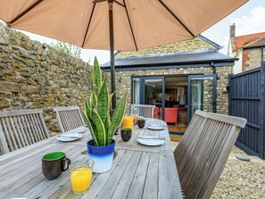 An outdoor dining area with a table, chairs, a potted plant, and a large umbrella.