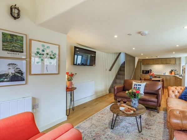 A modern living room with a sofa, a coffee table with snacks, a TV, and a staircase leading to a kitchen.