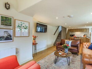 A modern living room with a sofa, a coffee table with snacks, a TV, and a staircase leading to a kitchen. - Coach House - UK32202 (Burton Bradstock, near Bridport)