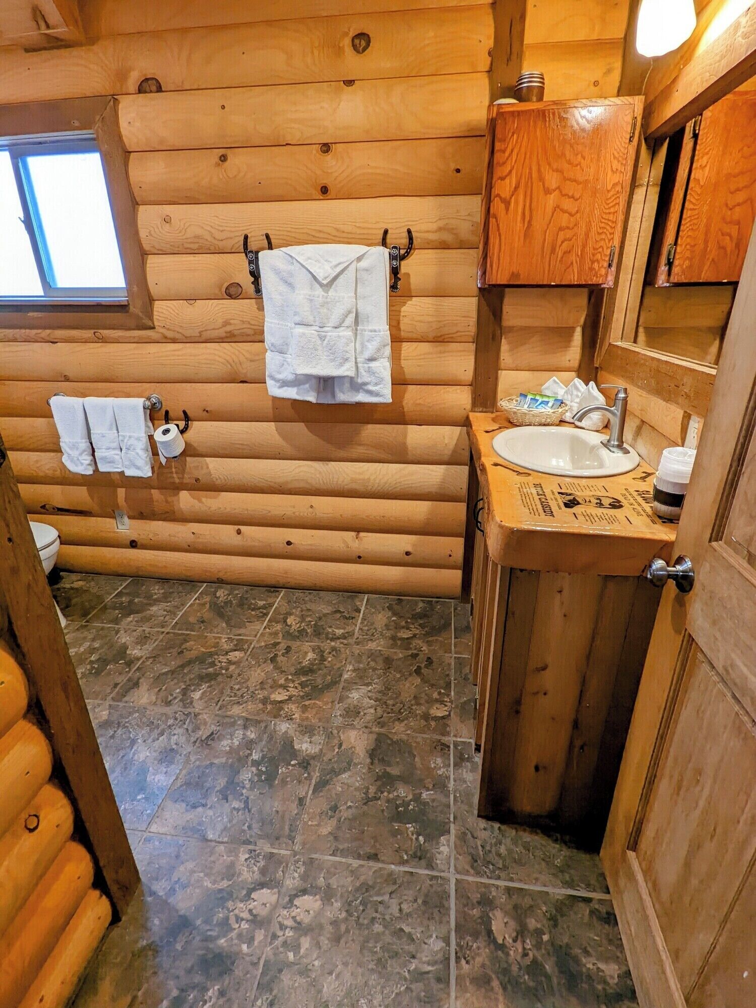 Une salle de bain rustique, aménagée dans une cabane en bois, avec un lavabo, un miroir et deux serviettes accrochées au mur.