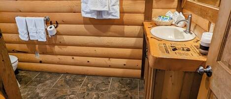 Une salle de bain rustique, aménagée dans une cabane en bois, avec un lavabo, un miroir et deux serviettes accrochées au mur.