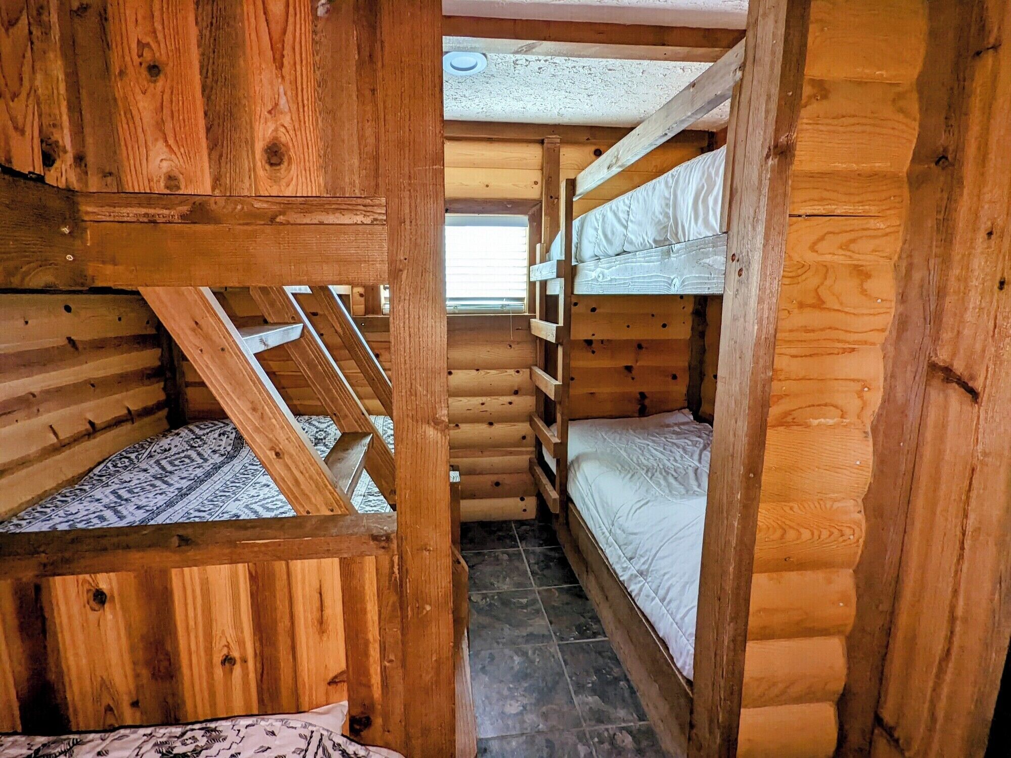 A wooden cabin with bunk beds, a sloped ceiling, and a window.