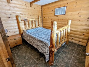 Una habitación de cabaña de madera con una cama, una mesita de noche y un ventanal pequeño.